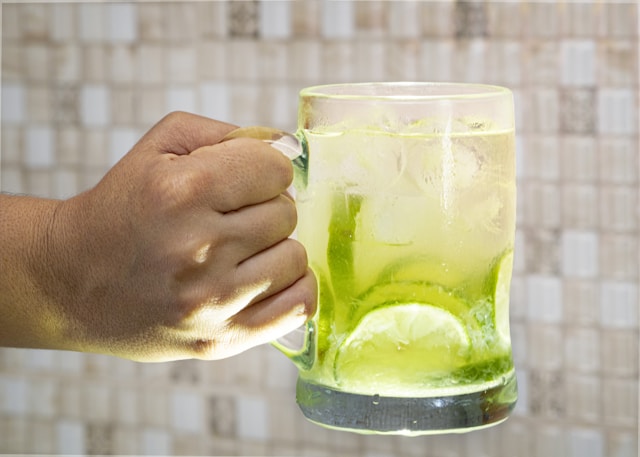 A person holding a mug of sliced limes in a drink